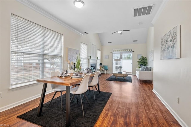 dining space with visible vents, baseboards, lofted ceiling, ornamental molding, and wood finished floors