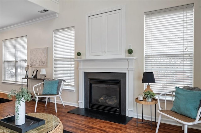 living room featuring visible vents, crown molding, baseboards, wood finished floors, and a glass covered fireplace