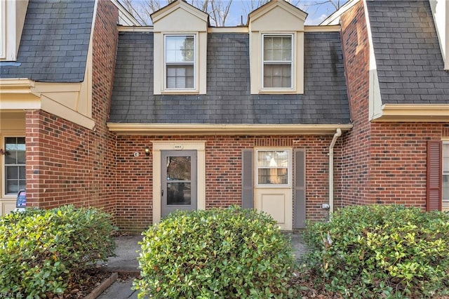 property entrance with mansard roof, brick siding, and roof with shingles