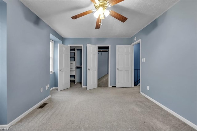 unfurnished bedroom with baseboards, visible vents, carpet floors, ceiling fan, and multiple closets