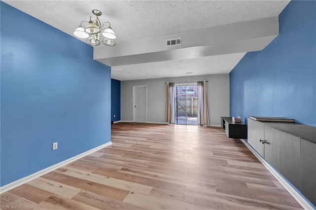 empty room with visible vents, baseboards, light wood-style floors, a notable chandelier, and a textured ceiling