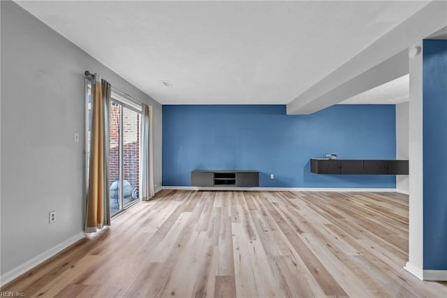 unfurnished living room featuring visible vents, baseboards, and wood finished floors