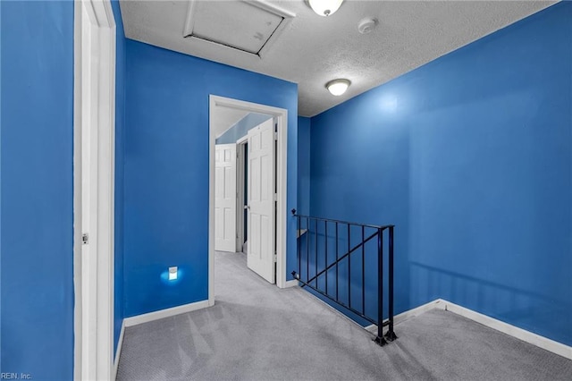 hall with baseboards, attic access, carpet floors, an upstairs landing, and a textured ceiling