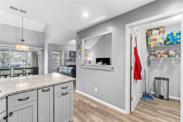 kitchen featuring visible vents, light wood-style flooring, light stone counters, decorative light fixtures, and baseboards