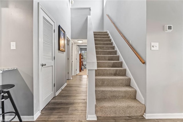 staircase featuring baseboards, wood finished floors, and a towering ceiling