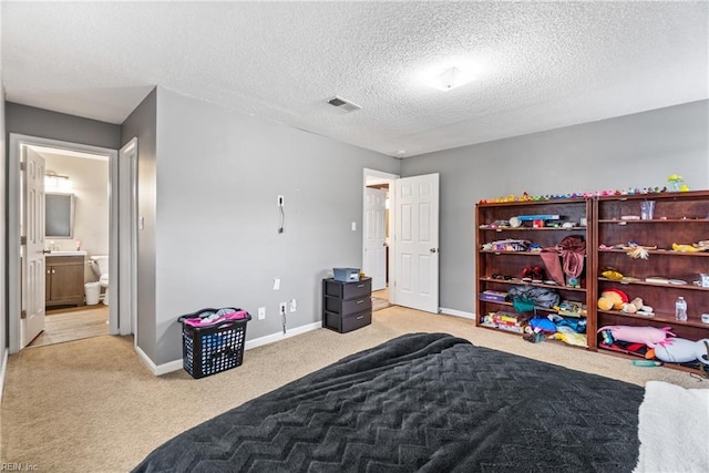 carpeted bedroom with ensuite bath, visible vents, a textured ceiling, and baseboards