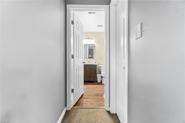 corridor with a sink, baseboards, visible vents, and light carpet