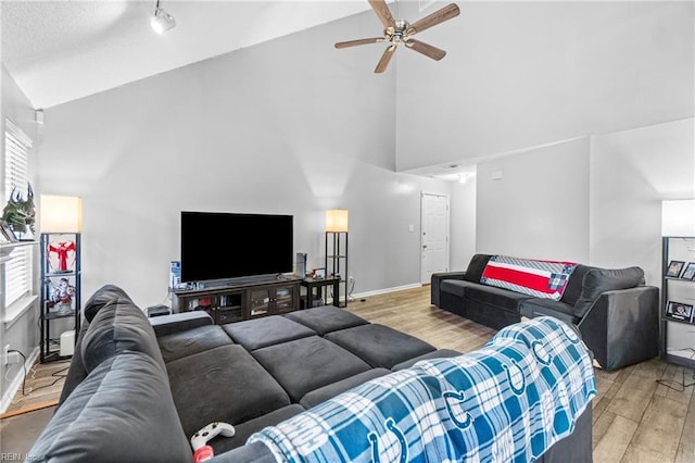 living area with light wood-type flooring, high vaulted ceiling, track lighting, a ceiling fan, and baseboards