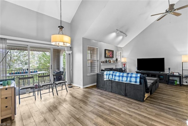 living area featuring a ceiling fan, wood finished floors, baseboards, high vaulted ceiling, and track lighting