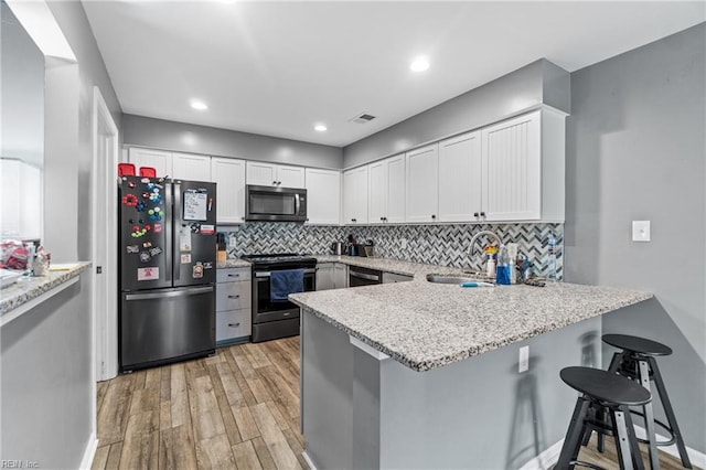 kitchen with visible vents, a sink, appliances with stainless steel finishes, a peninsula, and light wood finished floors