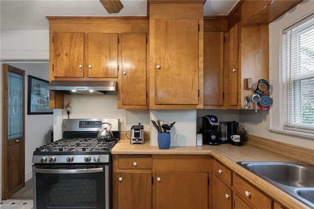 kitchen with a wealth of natural light, range hood, stainless steel gas range, and brown cabinetry