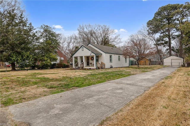 bungalow-style home featuring aphalt driveway, a front lawn, a detached garage, and an outdoor structure