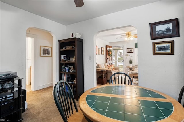 carpeted dining room featuring arched walkways and ceiling fan