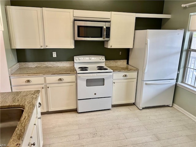 kitchen featuring light wood finished floors, light stone counters, white cabinets, white appliances, and a sink