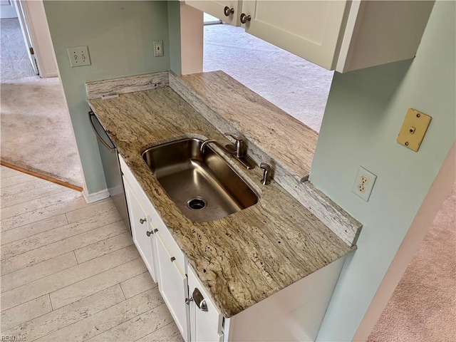 kitchen with white cabinets, light stone countertops, dishwasher, and a sink