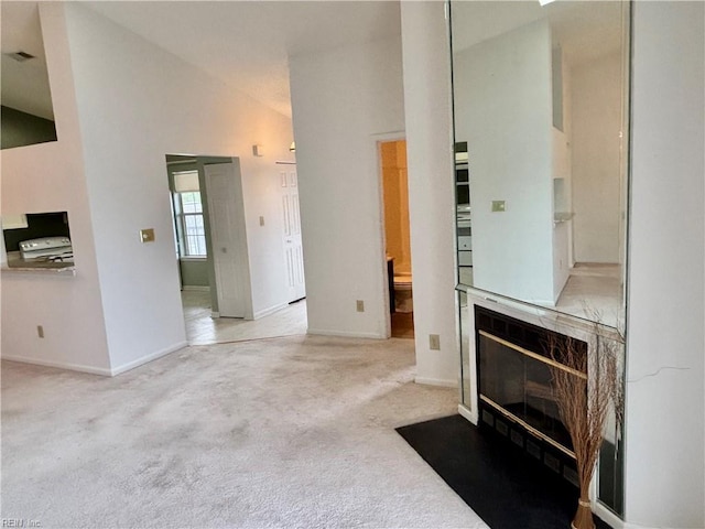 unfurnished living room featuring a fireplace with flush hearth, baseboards, carpet floors, and high vaulted ceiling