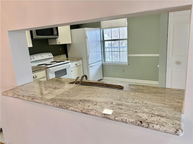 kitchen featuring light stone counters, white cabinets, white appliances, and a sink