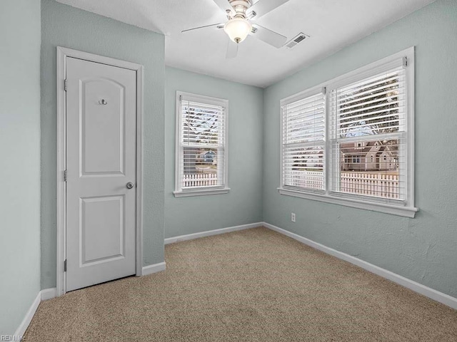 empty room featuring visible vents, baseboards, ceiling fan, carpet flooring, and a textured wall