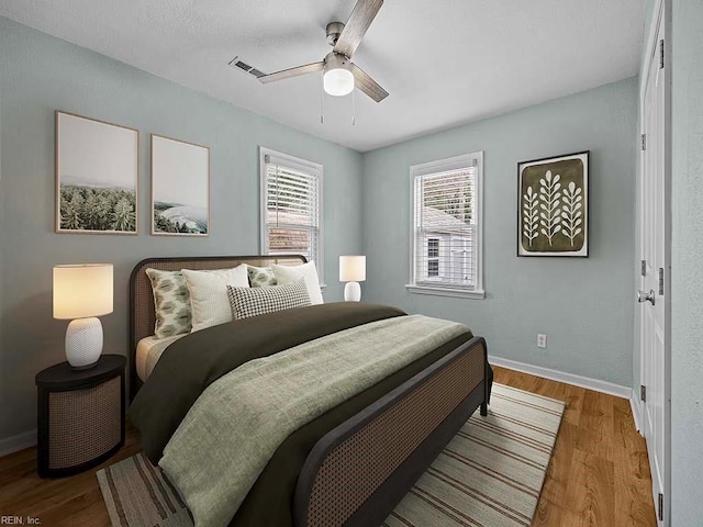 bedroom featuring ceiling fan, visible vents, baseboards, and wood finished floors