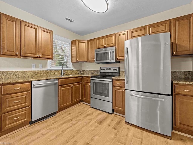 kitchen featuring visible vents, light wood-type flooring, a sink, stainless steel appliances, and brown cabinets