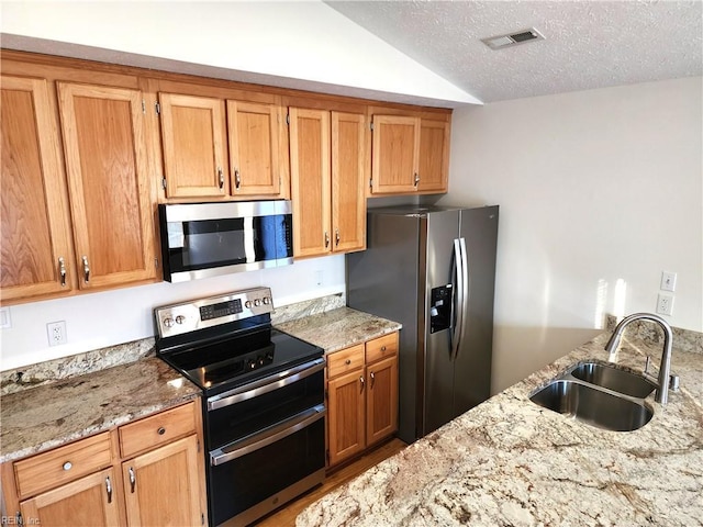 kitchen with visible vents, a sink, a textured ceiling, stainless steel appliances, and vaulted ceiling