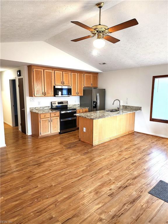 kitchen with light stone counters, a peninsula, light wood-style floors, stainless steel appliances, and a ceiling fan