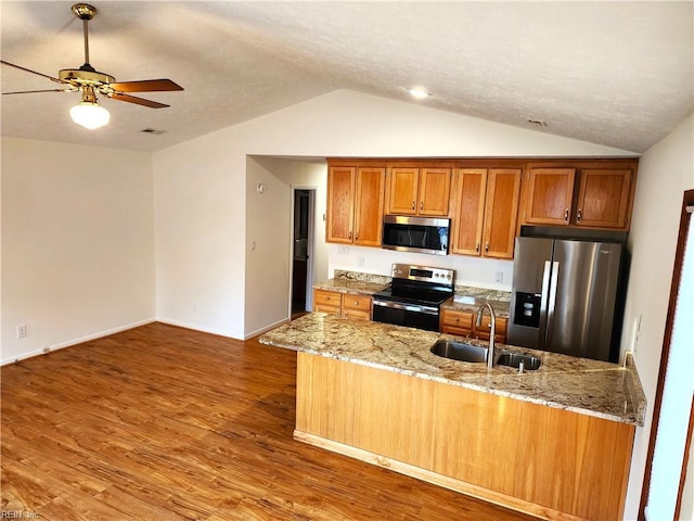 kitchen featuring a ceiling fan, wood finished floors, brown cabinetry, a sink, and appliances with stainless steel finishes