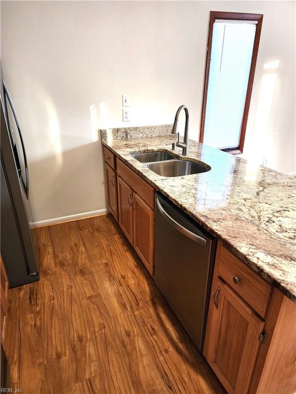 kitchen with dishwasher, dark wood-style floors, brown cabinets, and a sink