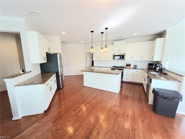 kitchen featuring a kitchen island, dark wood finished floors, dark stone counters, appliances with stainless steel finishes, and tasteful backsplash