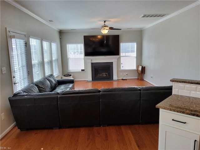 living room with plenty of natural light, wood finished floors, a ceiling fan, and ornamental molding