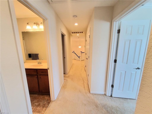 corridor featuring visible vents, light colored carpet, baseboards, and a sink