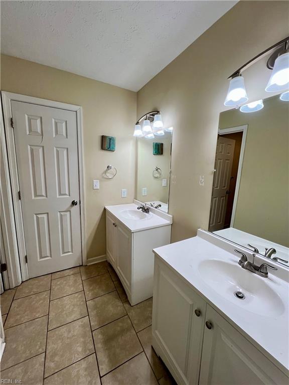 bathroom featuring tile patterned flooring, a textured ceiling, two vanities, and a sink