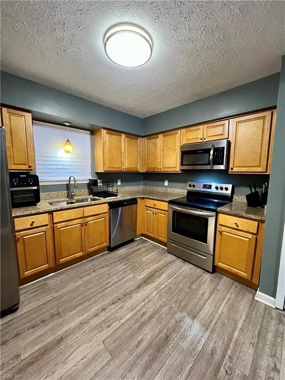 kitchen featuring a sink, stainless steel appliances, light wood-type flooring, and a textured ceiling