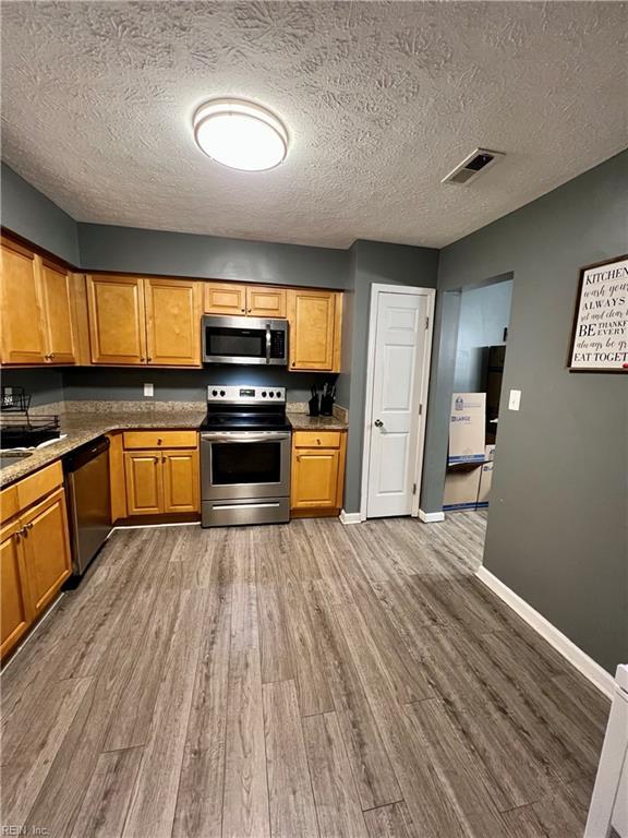 kitchen with visible vents, a textured ceiling, wood finished floors, appliances with stainless steel finishes, and baseboards