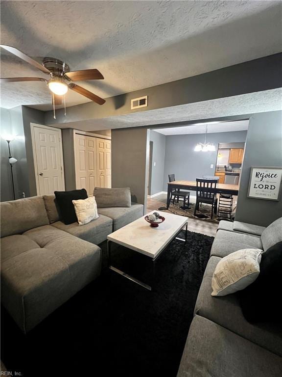 living room featuring visible vents, baseboards, ceiling fan, wood finished floors, and a textured ceiling