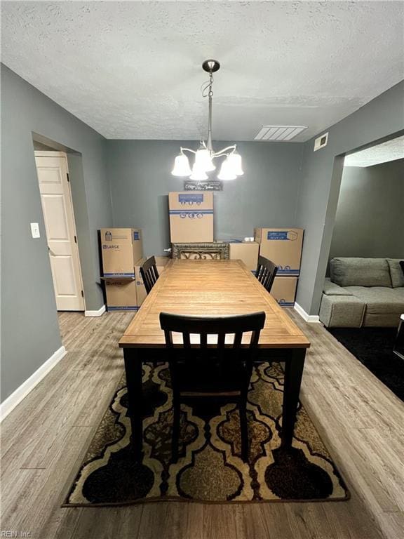 dining room featuring a textured ceiling, wood finished floors, baseboards, and a chandelier