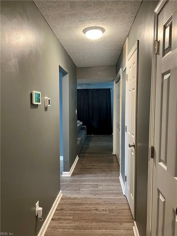 corridor with a textured ceiling, baseboards, and wood finished floors