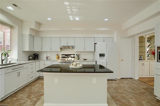 kitchen with stainless steel range with electric cooktop, a sink, white refrigerator with ice dispenser, under cabinet range hood, and a center island