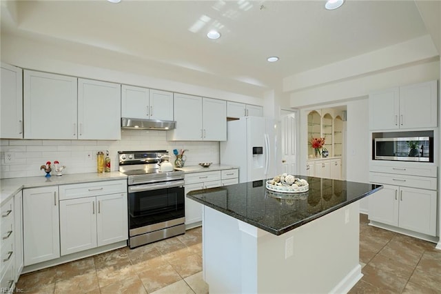 kitchen featuring under cabinet range hood, a center island, dark stone counters, appliances with stainless steel finishes, and decorative backsplash