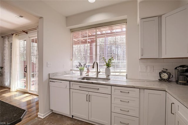 kitchen with a sink, tasteful backsplash, white cabinetry, light stone countertops, and dishwasher