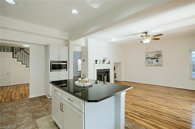 kitchen with wood finished floors, dark countertops, stainless steel microwave, open floor plan, and a center island