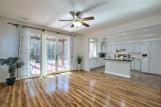 kitchen featuring visible vents, under cabinet range hood, decorative backsplash, white refrigerator with ice dispenser, and a ceiling fan