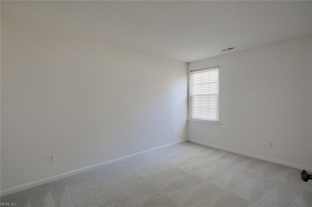 spare room featuring visible vents, light colored carpet, and baseboards