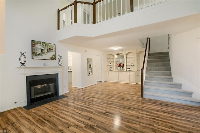 unfurnished living room featuring stairway, a fireplace with flush hearth, baseboards, and wood finished floors