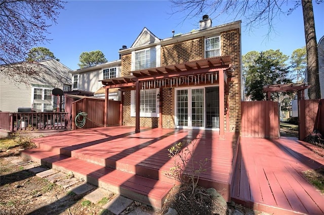 back of property with a deck, a pergola, brick siding, and a chimney