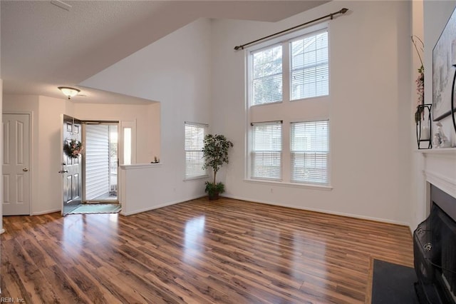 unfurnished living room with a fireplace with flush hearth, wood finished floors, baseboards, and a towering ceiling