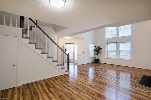 foyer entrance with baseboards, a textured ceiling, wood finished floors, and stairs