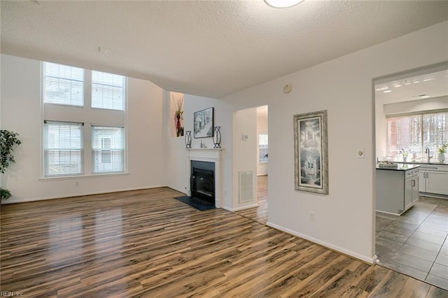 unfurnished living room featuring a fireplace with flush hearth, a textured ceiling, visible vents, and wood finished floors