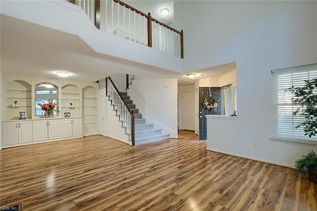 unfurnished living room featuring stairway, wood finished floors, and a towering ceiling