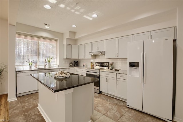 kitchen with under cabinet range hood, a sink, backsplash, white cabinetry, and white appliances